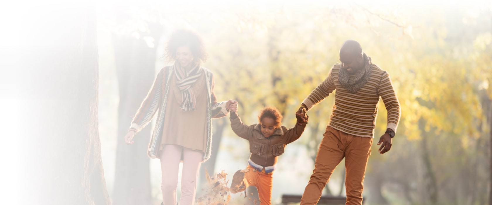 Family walking in park holding hands splashing leaves
