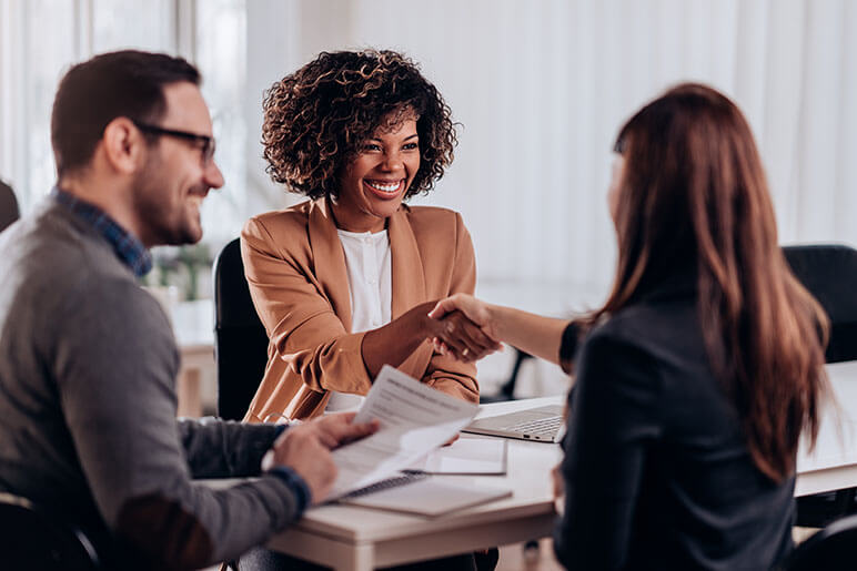 A woman who is an insurance agent shaking hands with two adults after looking over paperwork