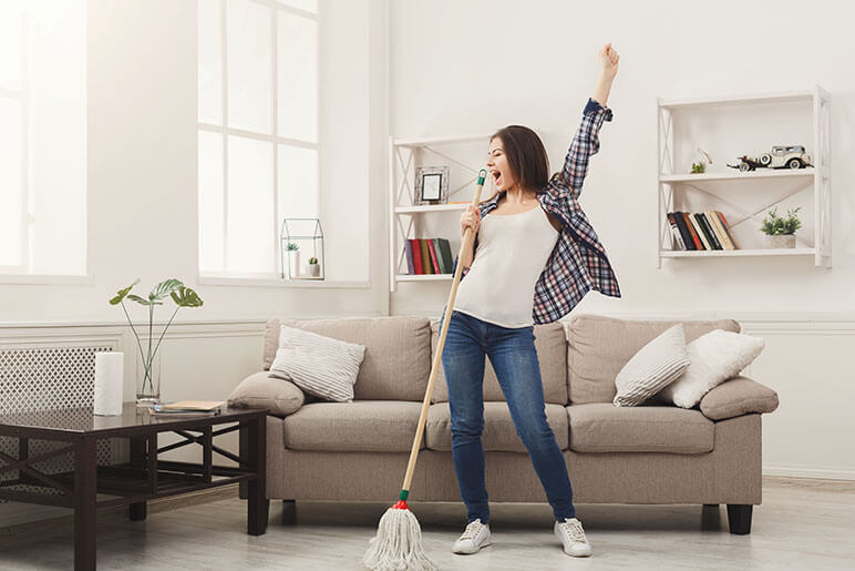 Woman in the living room holding a mop singing