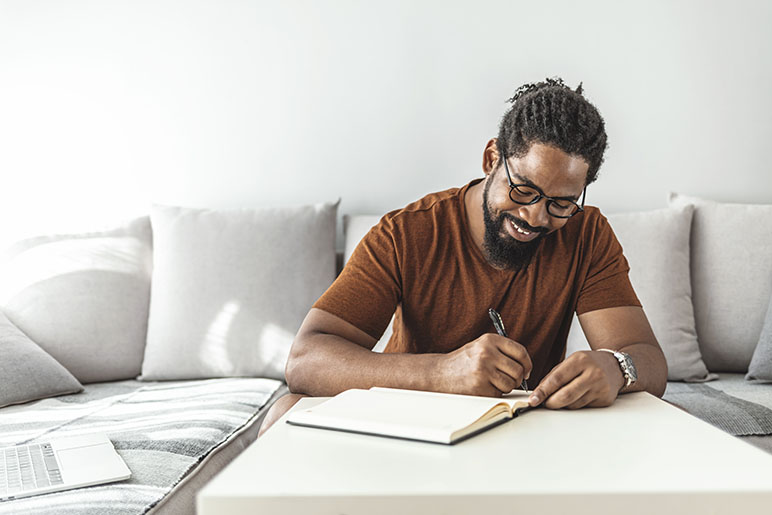 a man smiling and writing in his gratitude journal during the holiday season