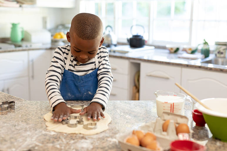 Young boy making cookies with cookie cutouts in the kitchen of his home