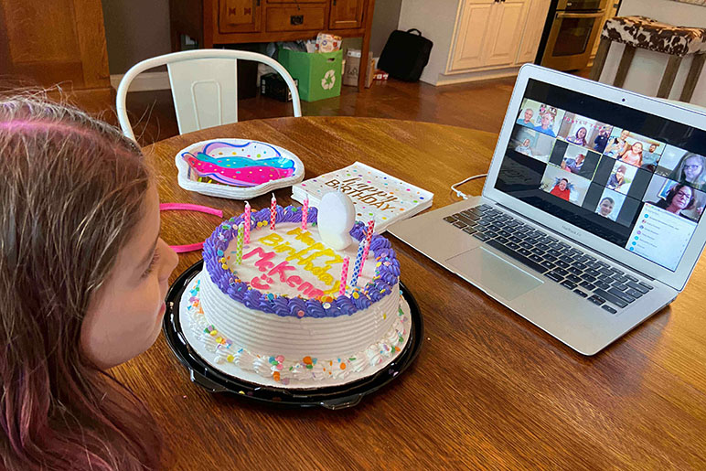 Girl celebrating her birthday with a cake and a computer with her friends on camera
