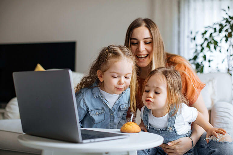 Mother with two daughters blowing out a candle in front of a laptop