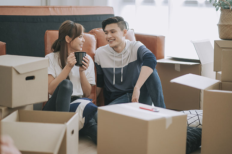 Couple sitting down unpacking cardboard boxes at their new apartment