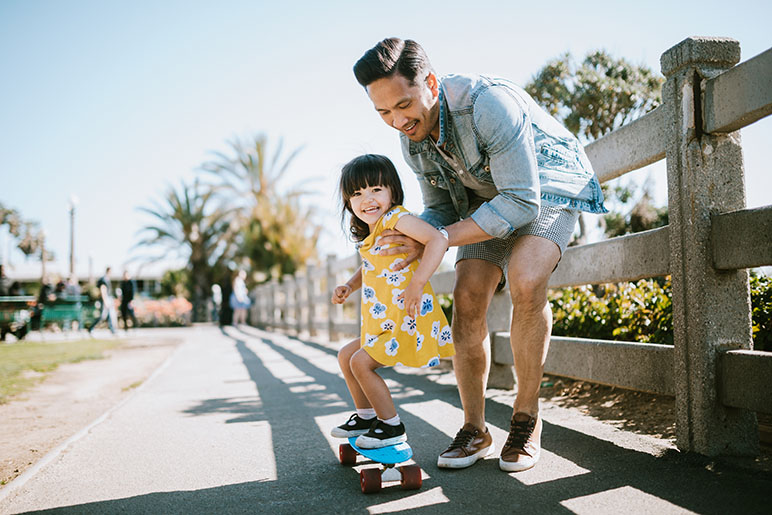 Dad and daughter riding on a skateboard on a sidewalk