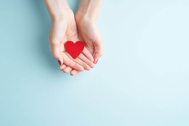 Two hands holding a red heart that have a light blue background