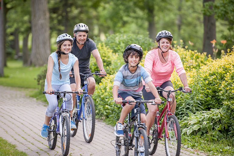 Family of four riding their bikes on a brick path with helmets on