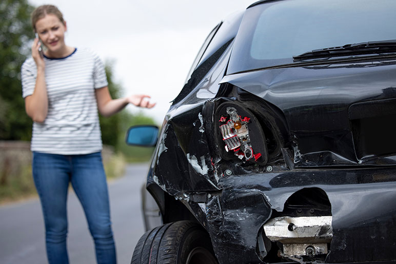 Girl standing by her car on the phone and the car has been rear-ended