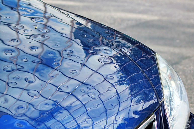 A blue hood of the car with hail damage on the top of it