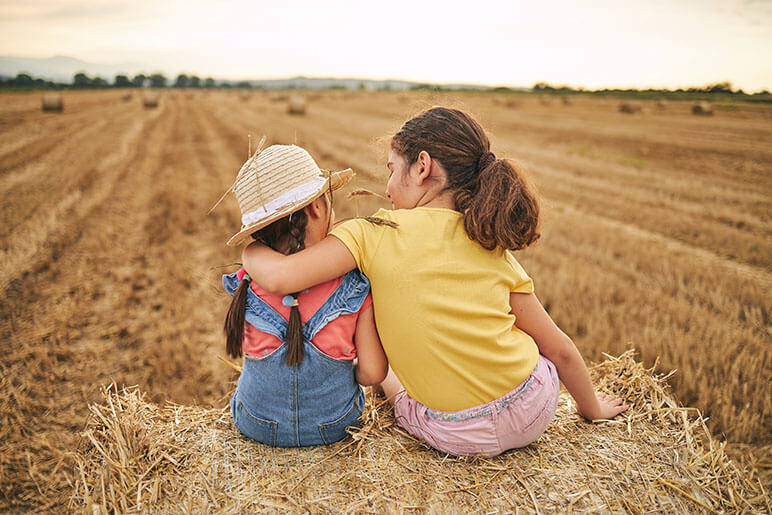 Two sisters seating on hay in the middle of a field on a farm