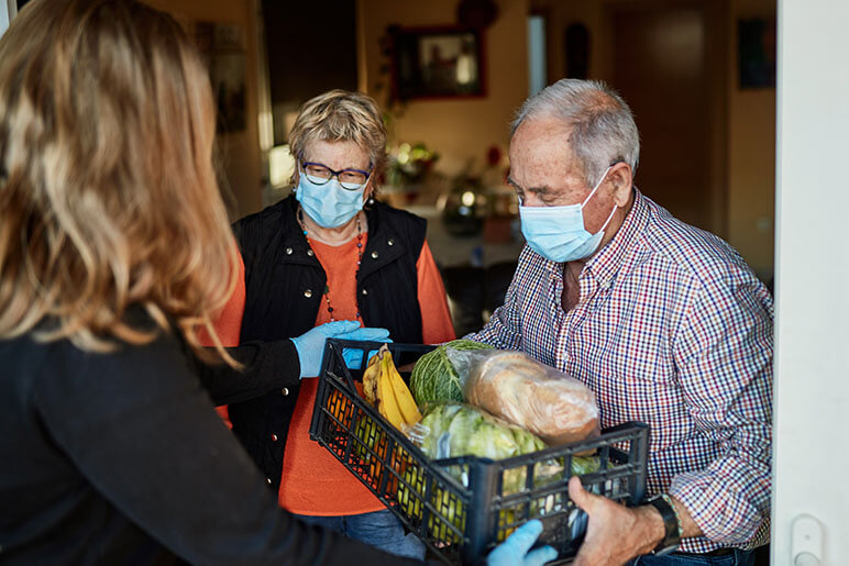 Woman delivering food to an elderly couple with masks on