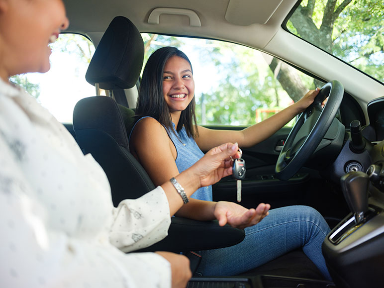 Young driver with woman in the passenger's seat being handed the keys for the car