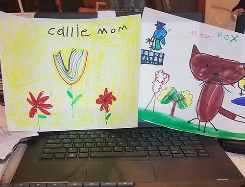 Someone's laptop with two of her daughter's drawings taped on the screen of her computer