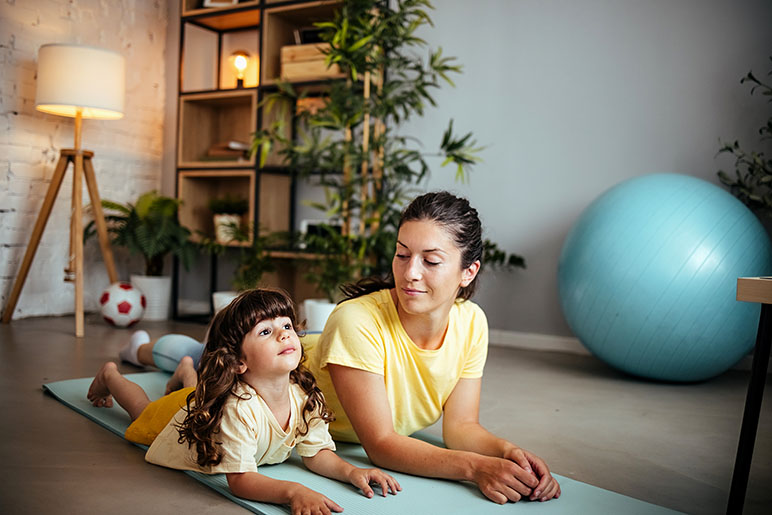 Mom and daughter doing yoga in living room for their mental health