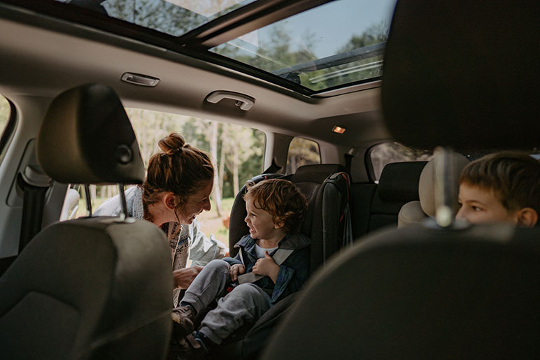 Mom getting her two children in the backseat of a car