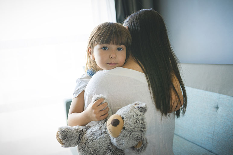 Older woman holding a smaller child in her arms with a teddy bear