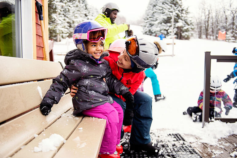 Mother and daughter sitting on a bench with snow gear on getting ready to ski, snowboard or tube