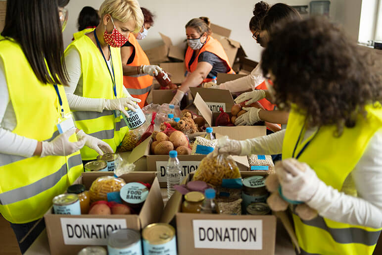 A group of individuals with volunteer vests on sorting food items into various donation boxes