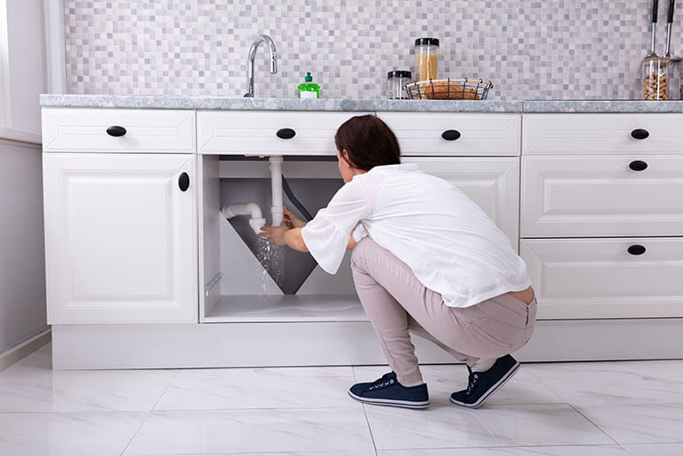 Woman trying to fix a water leak under her kitchen faucet