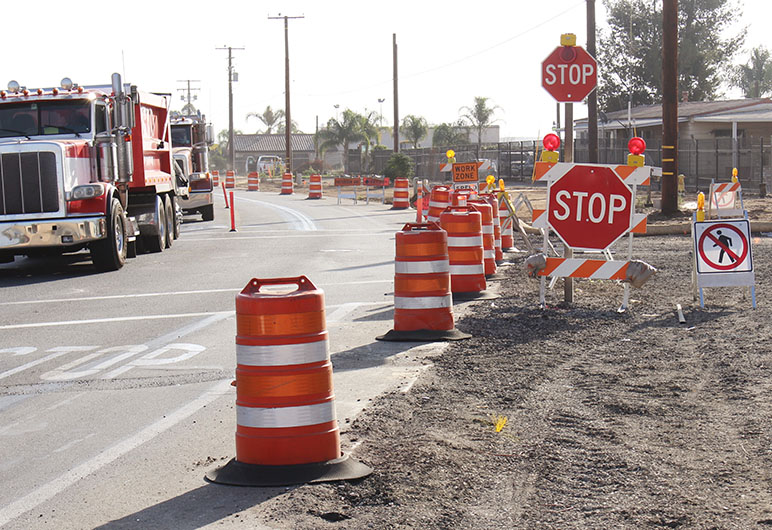 Photo of road construction on a street with orange traffic cones, red stop signs and two dump trucks