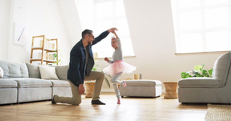 Father and daughter in the living room dancing with the father twirling the daughter around in a tutu