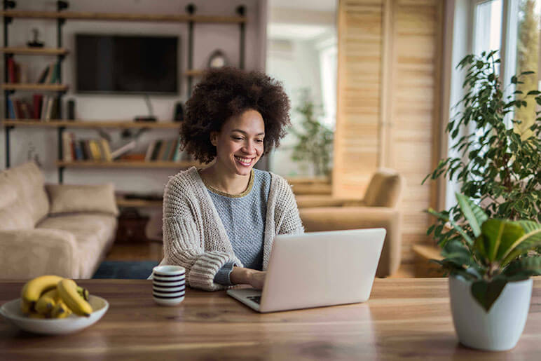 Woman smiling while using her computer at her kitchen table