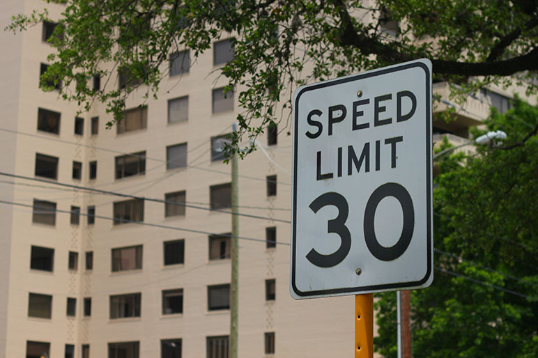 Speed limit sign that reads 30 mph by a office building and greenery