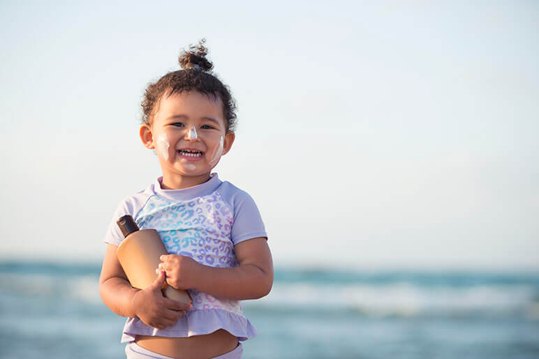 Little girl wearing sunscreen and holding a bottle of sunscreen