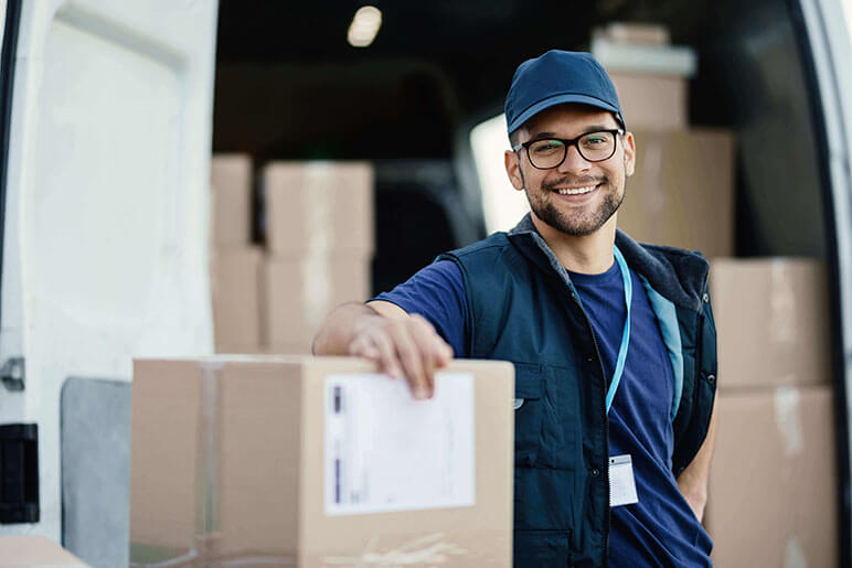 Delivery man smiling while leaning on a few boxes that he is delivering.  