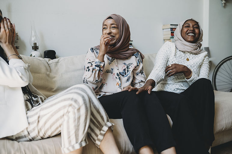 Three women sitting on the couch laughing and smiling with each other