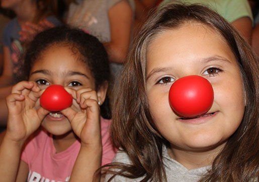 Two girls wearing red clown noses and smiling