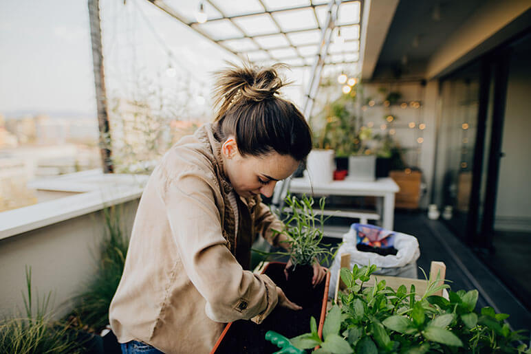 A woman planting plants on her balcony in the city demonstrating urban agriculture