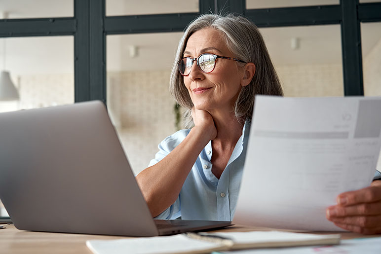 Woman looking over paper and her laptop on information regarding insurance