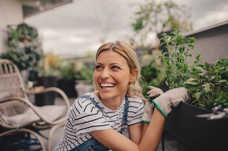 Woman smiling on her balcony next to her herb garden