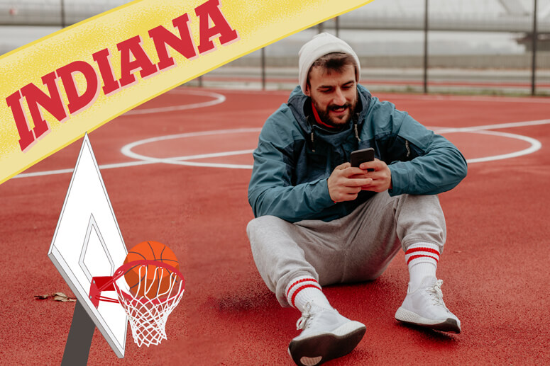 Young man on the basketball court outside on his phone with a basketball hoop graphic and Indiana banner