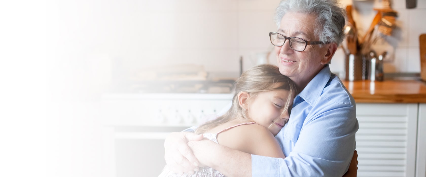 Senior woman hugging child at home. Happy family enjoying kindness, support, care together in cozy kitchen-min