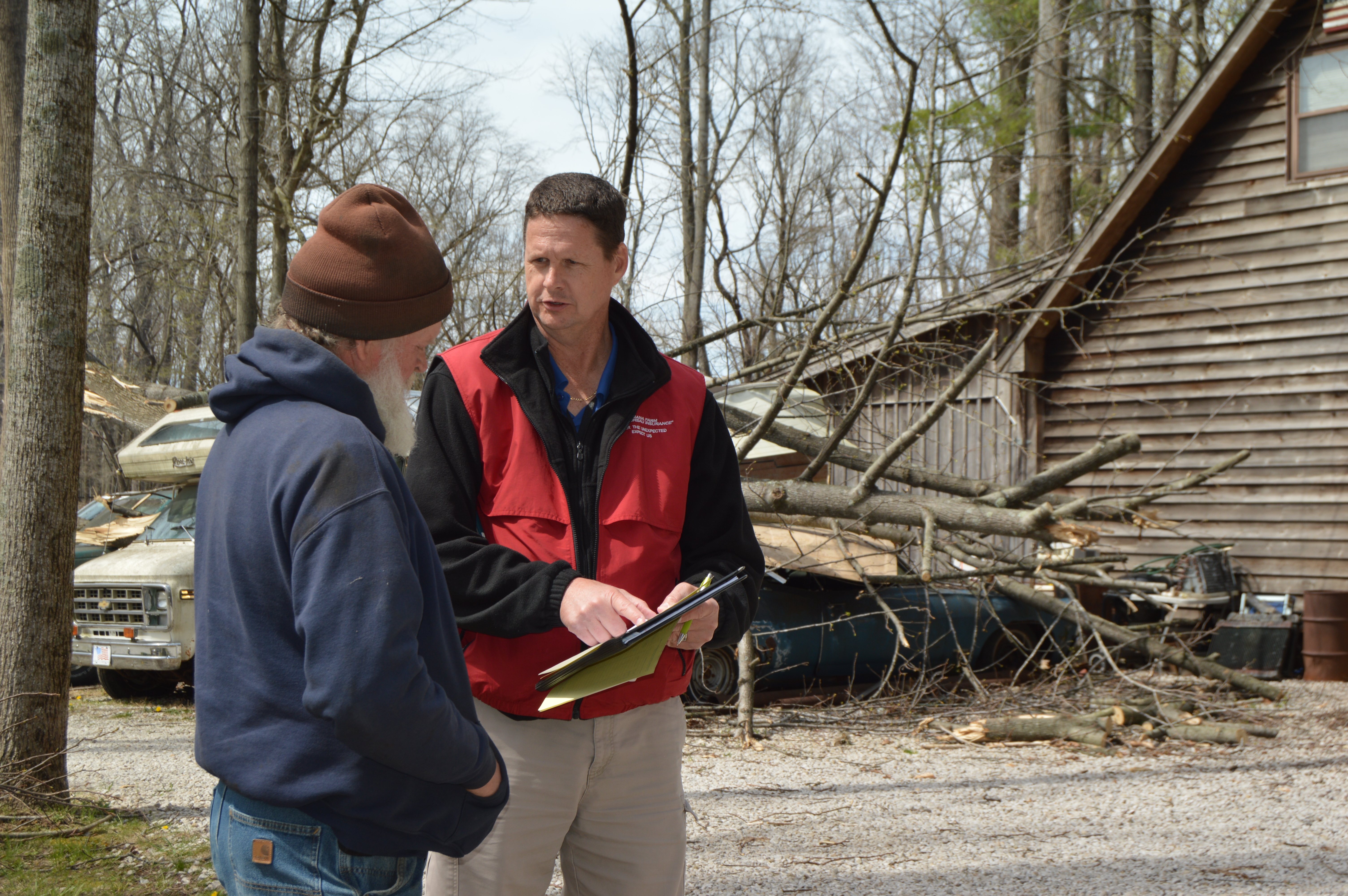 An Indiana Farm Bureau Insurance claims representative talks with a client. In the background a tree is lying on a crushed car.